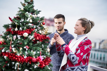 Young couple decorating Christmas tree on balcony