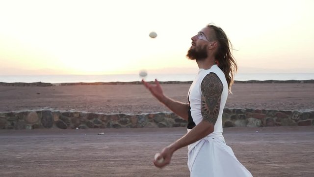Tattooed handsome man in profile make juggling show at sunset shaky footage