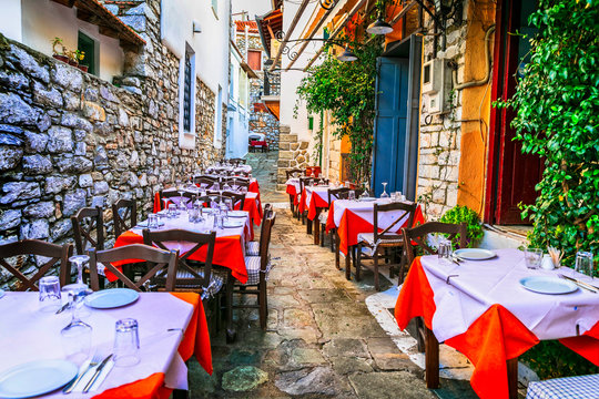 Traditional Greek taverna in narrow street of Skiathos island with red tablecloths and brick walls charming mediterranean restaurant outdoor terrace Greece travel destination scenic town