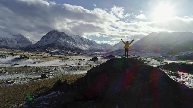 Male mountain climber raising hands with icepick on top of snowy peak