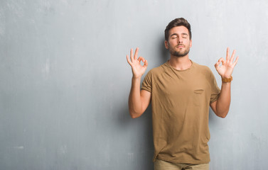 Handsome young man over grey grunge wall relax and smiling with eyes closed doing meditation gesture with fingers. Yoga concept.