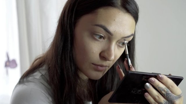 Beautiful young woman putting on make up in close up shot.