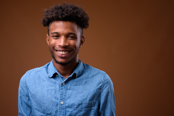 Happy young African man smiling against brown background