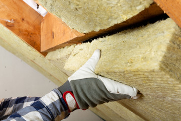 Man installing thermal roof insulation layer - using mineral wool panels. Attic renovation and...