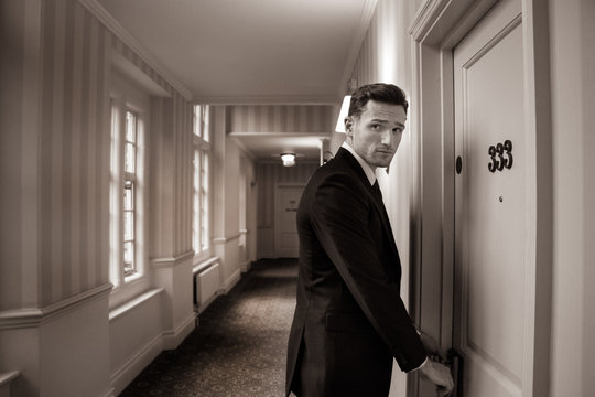 Sepia image of handsome man in suit in hotel corridor using key card to open room door