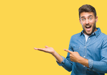 Young handsome man over isolated background amazed and smiling to the camera while presenting with hand and pointing with finger.