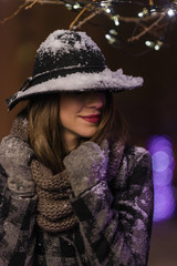 Young girl standing in front of christmas tree lights at night with snowflakes falling, snowing