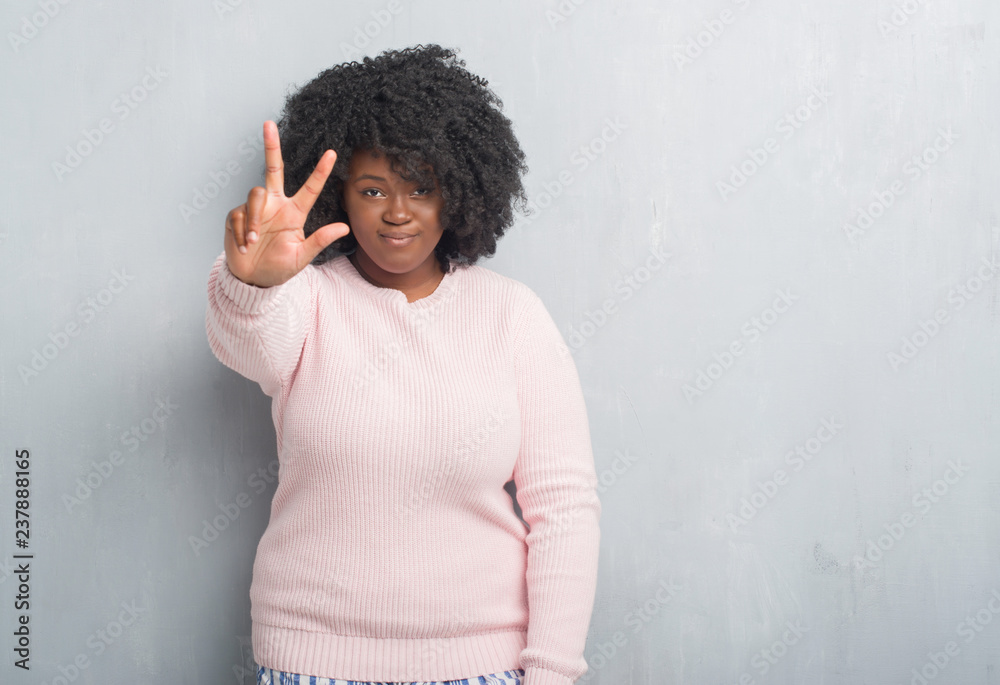 Wall mural young african american plus size woman over grey grunge wall wearing winter sweater showing and poin