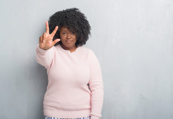 Young african american plus size woman over grey grunge wall wearing winter sweater showing and...