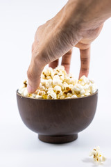 Hand grab popcorn in wooden bowl isolated on white background. Selective focus.