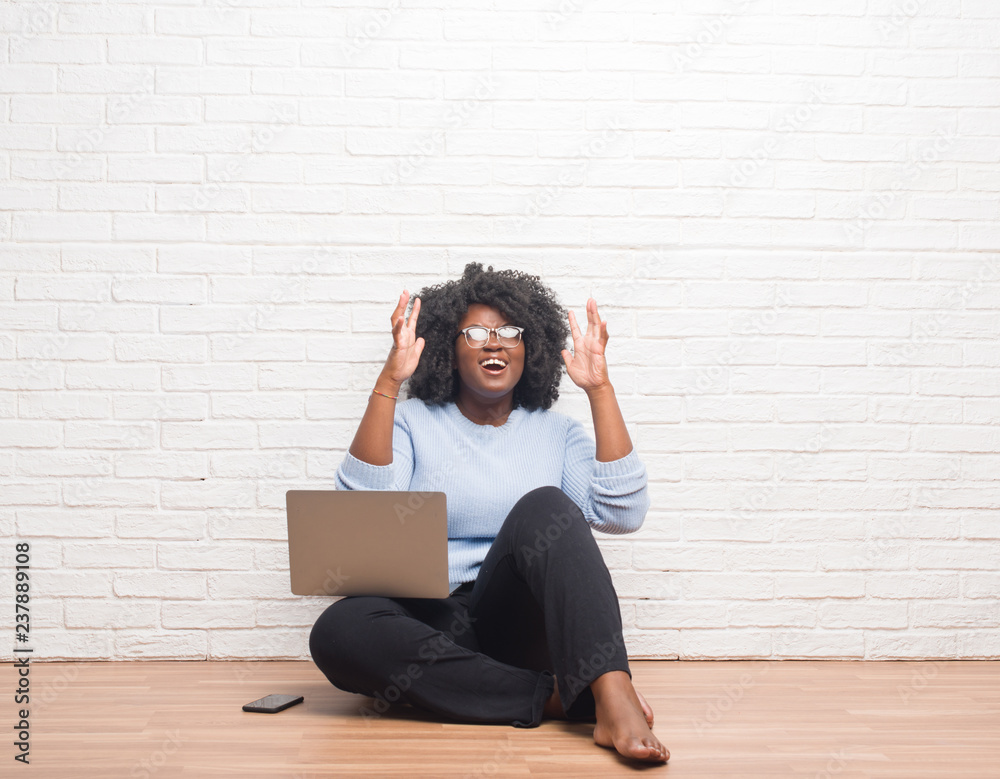 Canvas Prints Young african american woman sitting on the floor using laptop at home crazy and mad shouting and yelling with aggressive expression and arms raised. Frustration concept.