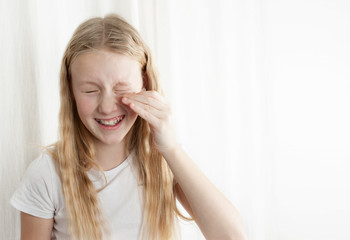 oung  girl  with curly and blonde hair trying on her mother's moisturizing patches from edema and tired eyes. Isolated photo on white background. Dust gets into girl's eyes. Free space copy for text