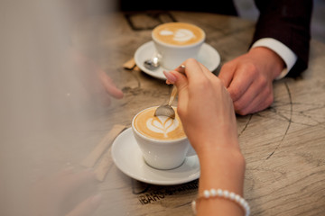 bride and groom hold cups with cappuccino and look at each other