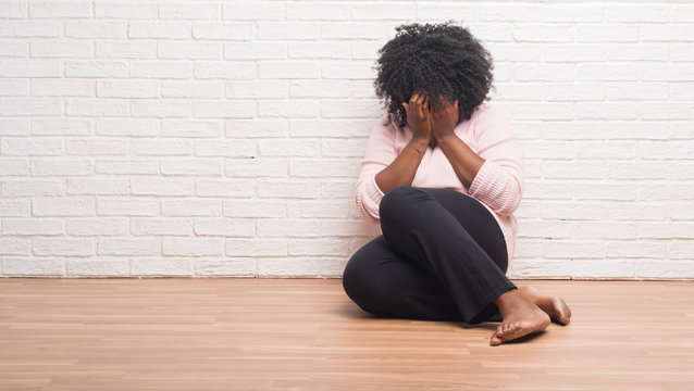 Young african american woman sitting on the floor at home with sad expression covering face with hands while crying. Depression concept.