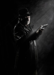 A private detective with a revolver in front of a black backdrop.