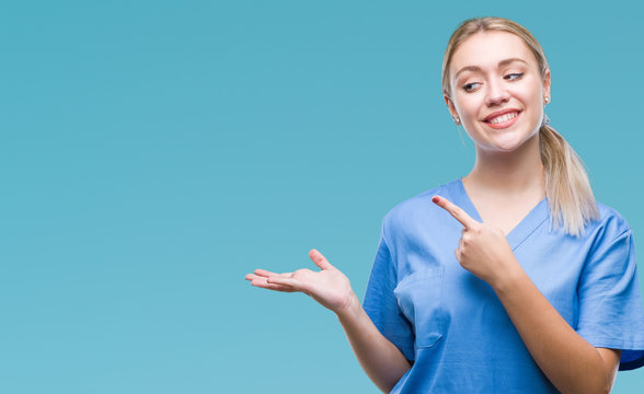 Young blonde surgeon doctor woman wearing medical uniform over isolated background amazed and smiling to the camera while presenting with hand and pointing with finger.