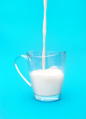 Milk pouring into the glass cup on blue background.