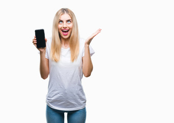Young beautiful blonde woman showing smartphone over isolated background very happy and excited, winner expression celebrating victory screaming with big smile and raised hands