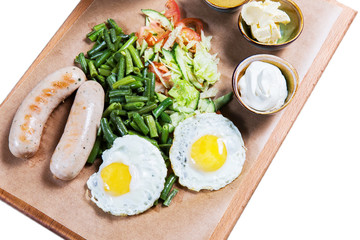 Omelette with sausages and vegetables on wooden cutting board on white background. English breakfast