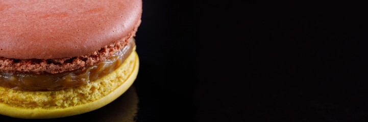 Bright juicy delicious macarons of two colors on a black background. Banner.
