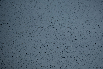 Regentropfen auf einer Fensterscheibe vor grauem Dezembermorgen