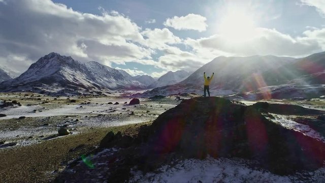 Male mountain climber raising hands with icepick on top of snowy peak