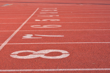 White numbers on starting line of a running track field, 1-8, with straight white lines divided each track equally.