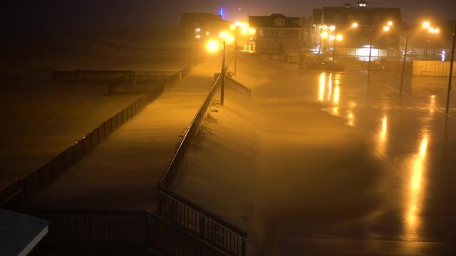 Very windy storm blows sand and rain around on an empty night beach boardwalk and parking lot.