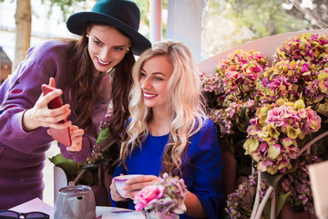 Two beautiful young women looking at the phone in the restaurant outdoor