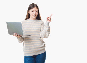 Young Chinese woman over isolated background using computer laptop very happy pointing with hand and finger to the side