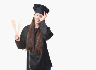 Young Chinese woman over isolated background wearing chef uniform with happy face smiling doing ok sign with hand on eye looking through fingers