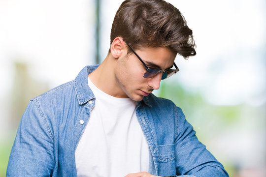 Young handsome man wearing sunglasses over isolated background Checking the time on wrist watch, relaxed and confident