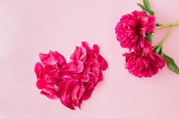 Flat lay heart composition with red petals and red peonies on a light pink background