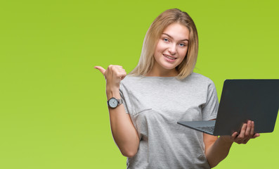 Young caucasian woman using computer laptop over isolated background pointing and showing with thumb up to the side with happy face smiling