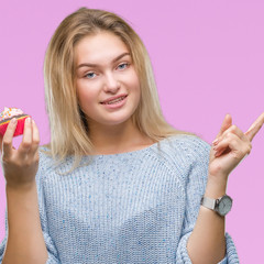 Young caucasian woman eating sweet cupcake over isolated background very happy pointing with hand and finger to the side