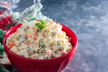 Traditional Russian New Year's salad in a red bowl with New Year's decor, horizontal, copy space