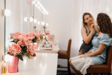 Beautiful roses in vase in beauty salon, female doing makeup on the background
