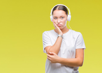 Young caucasian woman listening to music wearing headphones over isolated background thinking...
