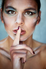 Creative personality with makeup, paint smears on the face. He puts his finger to his lips . Sign Shh
