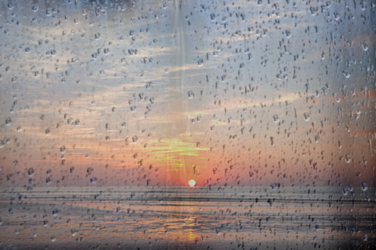 sun sets over the sea in holland seen through raindrops on window pane