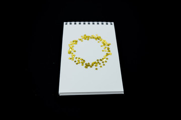Spiral Notebook, realistic mockup White scetchbook on black abstract background with golden stars confetti.Horizontal top view..
