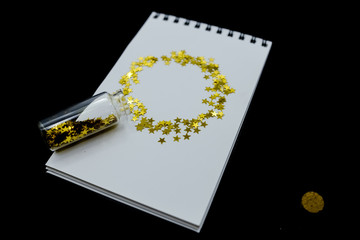 Spiral Notebook, realistic mockup White scetchbook on black abstract background with golden stars confetti.Horizontal top view..