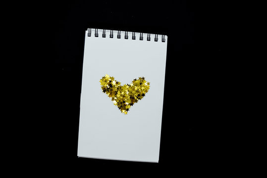 Spiral Notebook, realistic mockup White scetchbook on black abstract background with golden stars confetti.Horizontal top view..