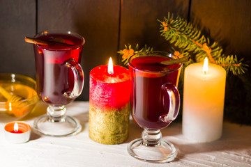 Mulled wine and burning candle on dark background. Christmas mulled wine, cinnamon sticks and honey. Alcohol drink of wine and honey. Festive drink and Christmas tree branches