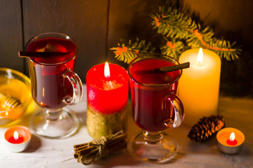 Mulled wine and burning candle on dark background. Christmas mulled wine, cinnamon sticks and honey. Alcohol drink of wine and honey. Festive drink and Christmas tree branches