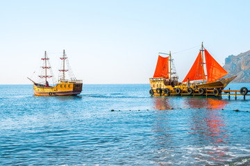Obraz premium Two old wooden ships. One of them with red sails on the pier.