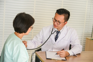 Asian male doctor using medical headphones or Stethoscope for Heart rate monitor Patients in the elderly to diagnose the symptoms of patients, to medical and health concept.