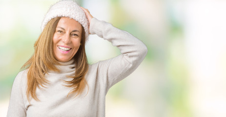 Beautiful middle age woman wearing winter sweater and hat over isolated background Smiling confident touching hair with hand up gesture, posing attractive