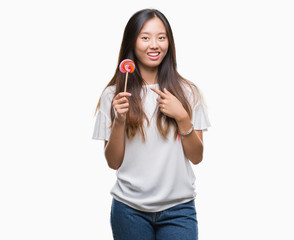 Young asian woman eating lollipop candy over isolated background very happy pointing with hand and...