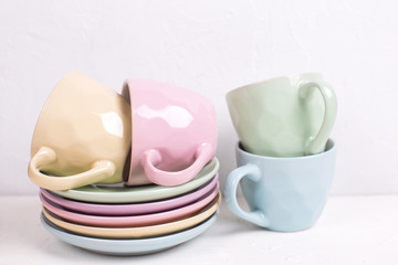 Pile of colourful tea cups and saucers on white textured background.